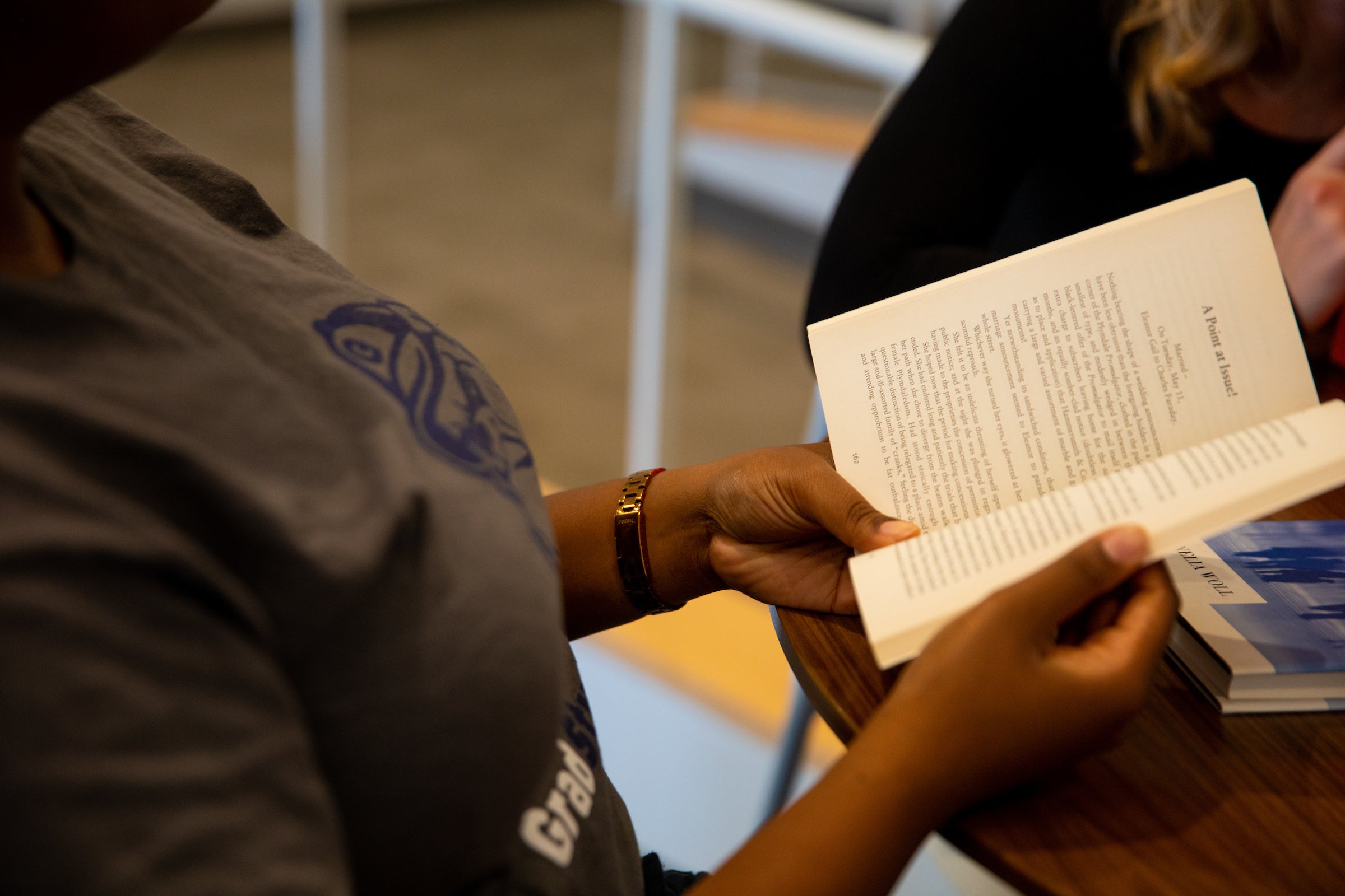 Individual in a Georgetown t-shirt reading a book at a table with another individual
